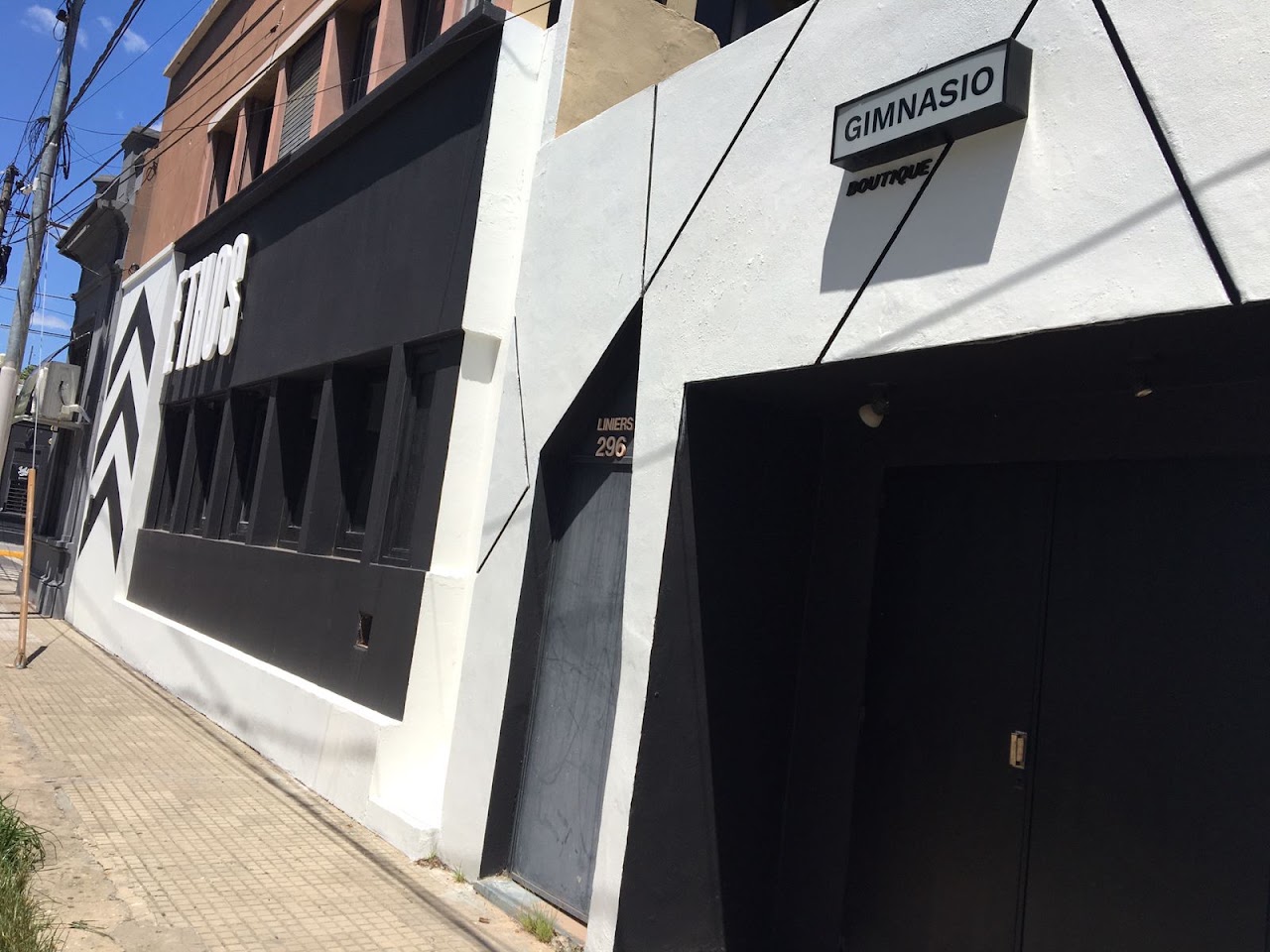 Modern premium boutique gym storefront facade exterior in Paraná Argentina, architectural photo, minimalist black and white diagonal chevron signage with wordmark ETHOS